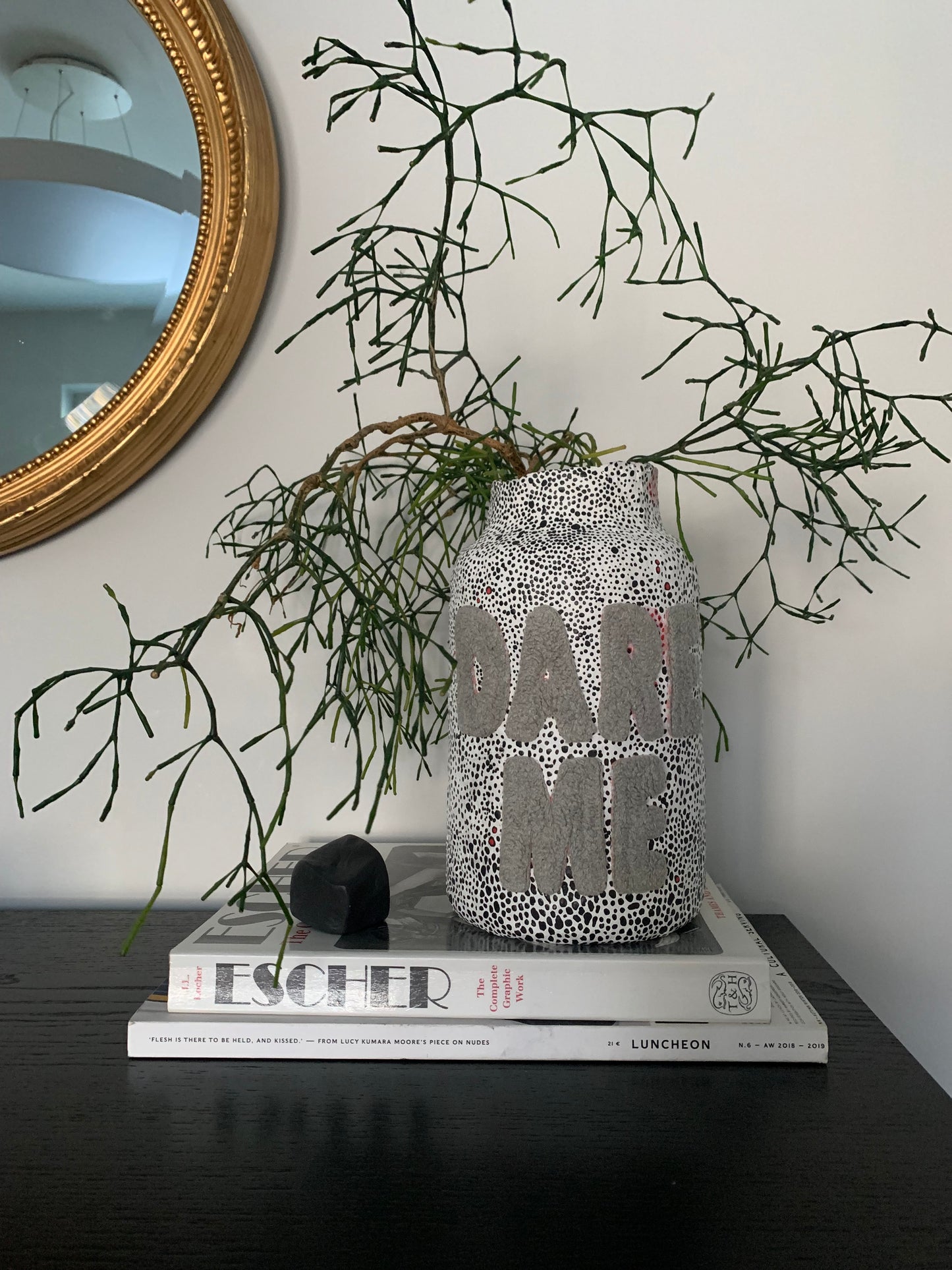 paper mache vase of a cylindrical shape with tapered neck. The vase is decorated with black and white dot pattern scattered across white background. Large bold letters spelling "DARE ME" attached to the front of the vase, creating a sttriking contrast. 