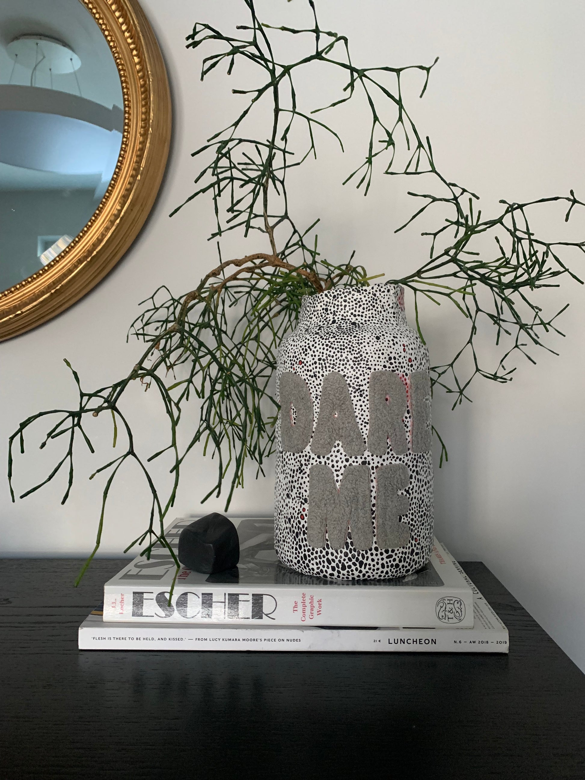 paper mache vase of a cylindrical shape with tapered neck. The vase is decorated with black and white dot pattern scattered across white background. Large bold letters spelling "DARE ME" attached to the front of the vase, creating a sttriking contrast. 